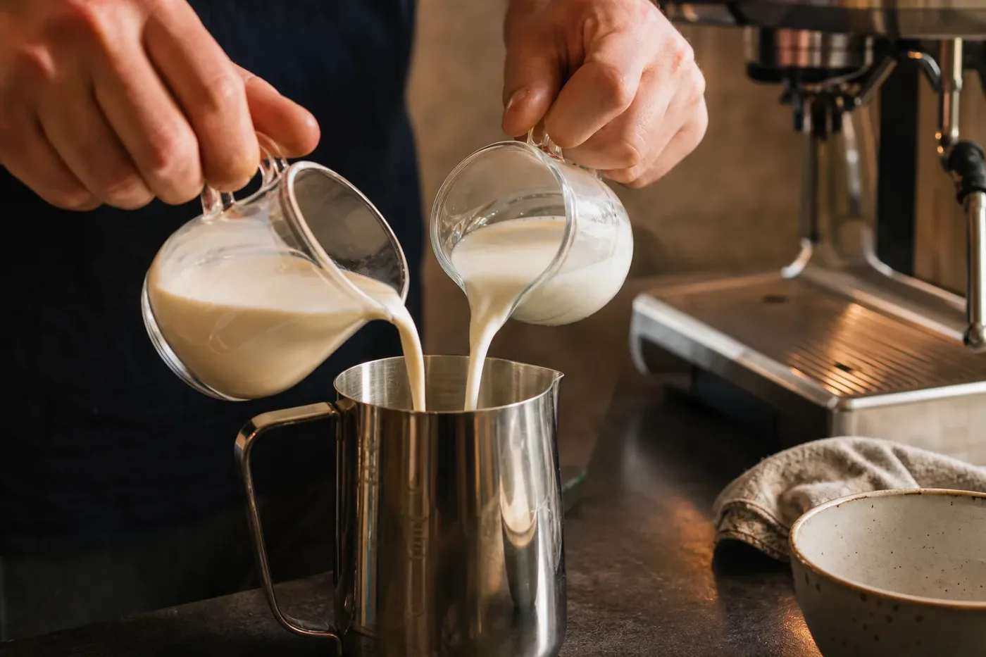 Milk and cream poured into a steel pitcher to make half and half for a breve