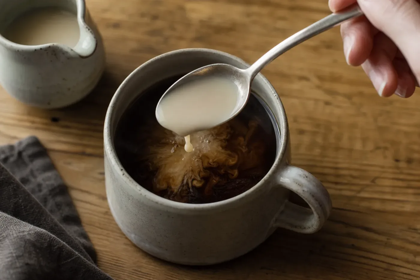 Coffee creamer swirling into a mug of black coffee