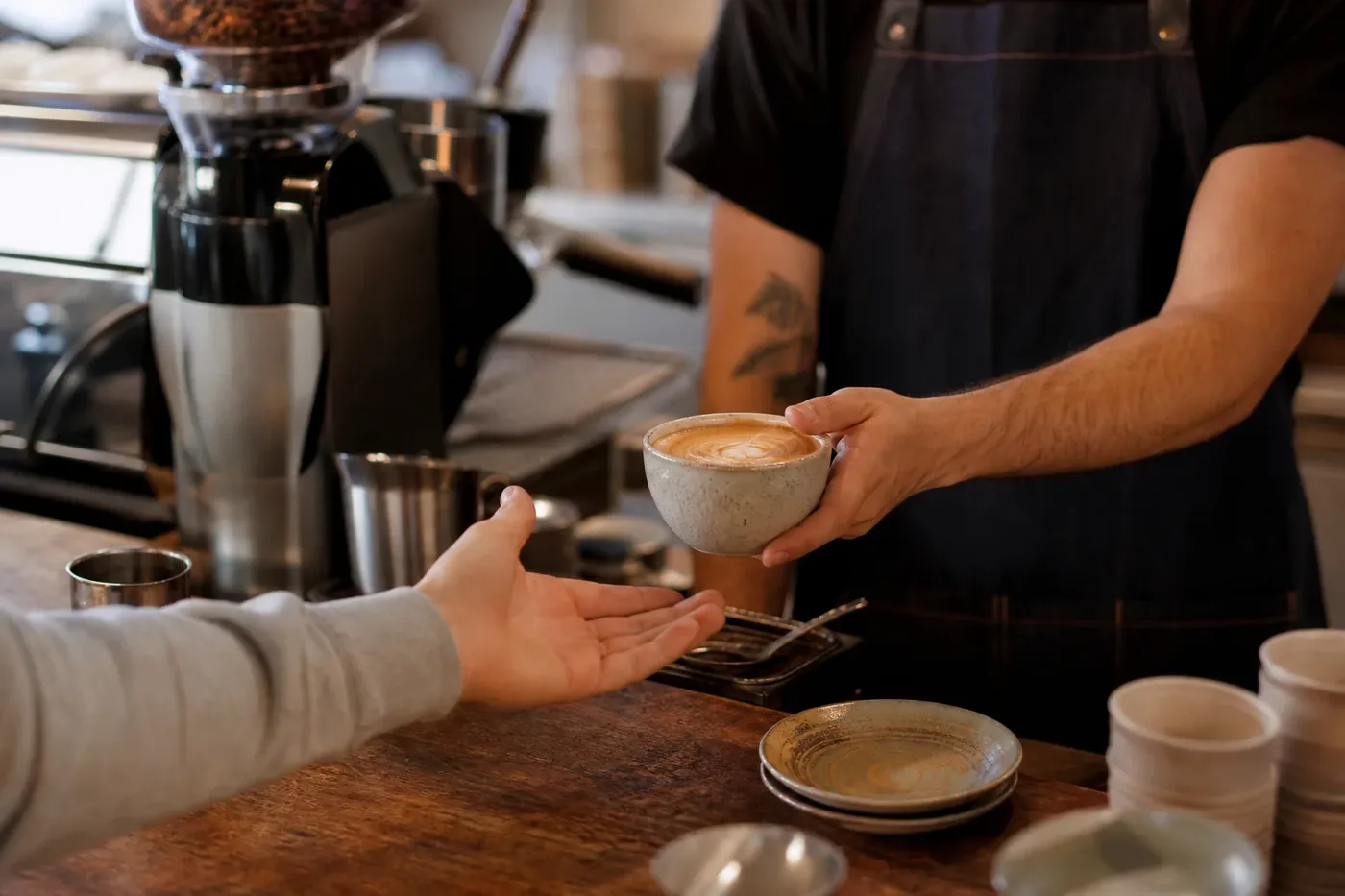 A barista handing a coffee across a busy cafe counter to a customer