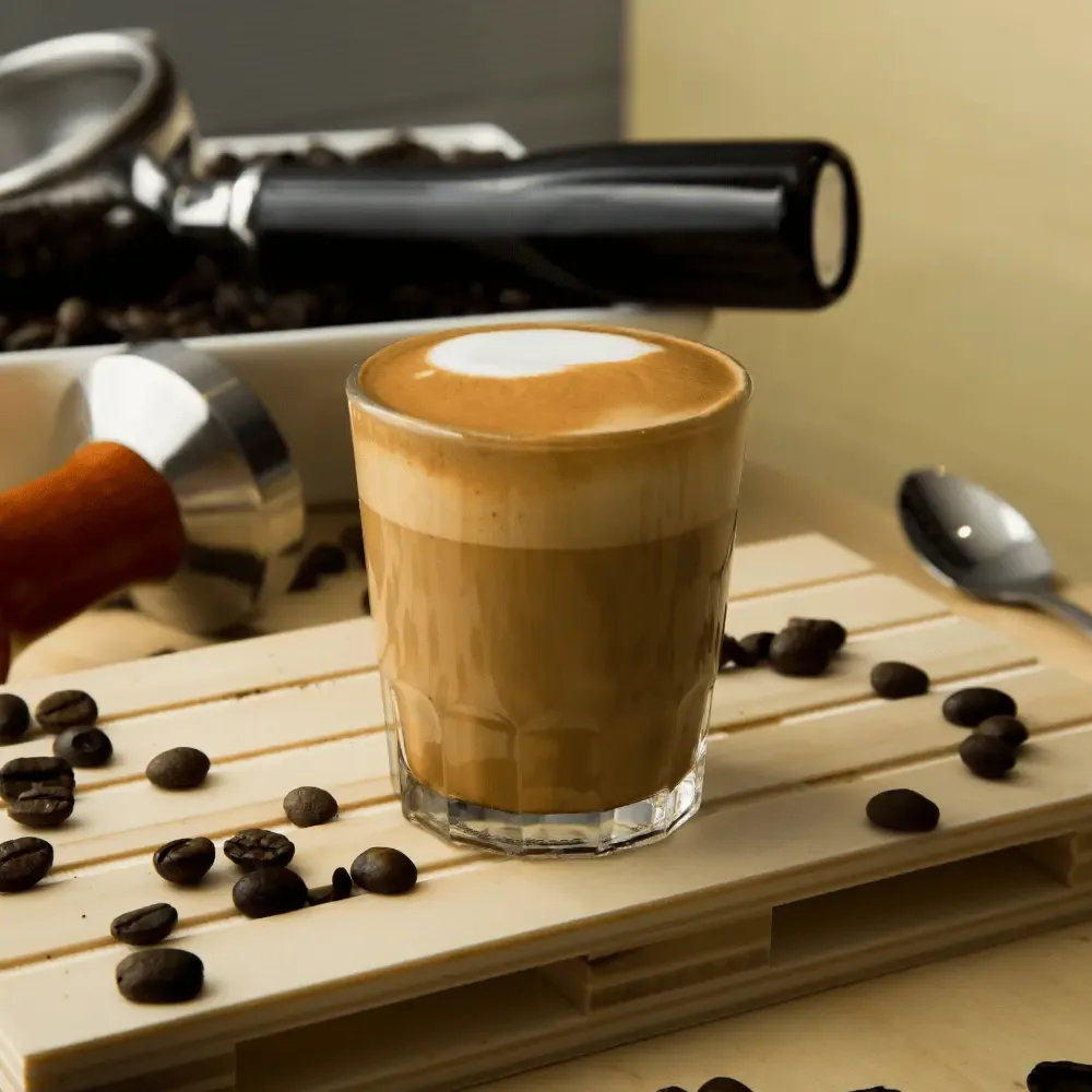 Cortado coffee in a glass on a board with beans