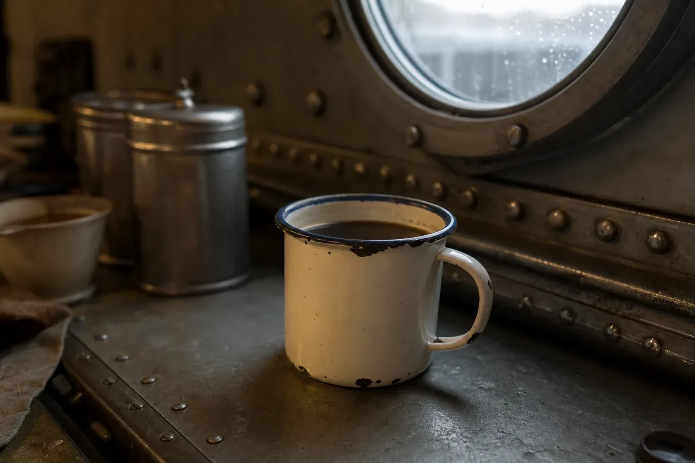 An enamel mug of black coffee on a steel table in a wartime ship's mess