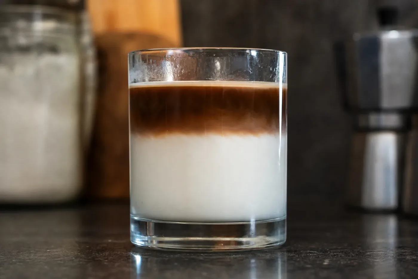 A dirty coffee in a clear glass, a band of dark espresso sitting on cold milk without mixing
