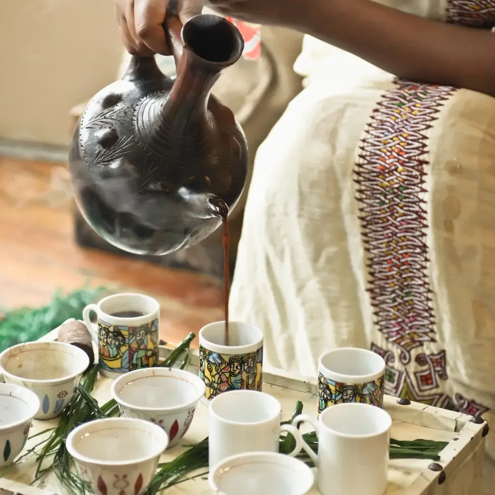 Small handleless cups arranged on a tray beside a clay jebena for the first round.