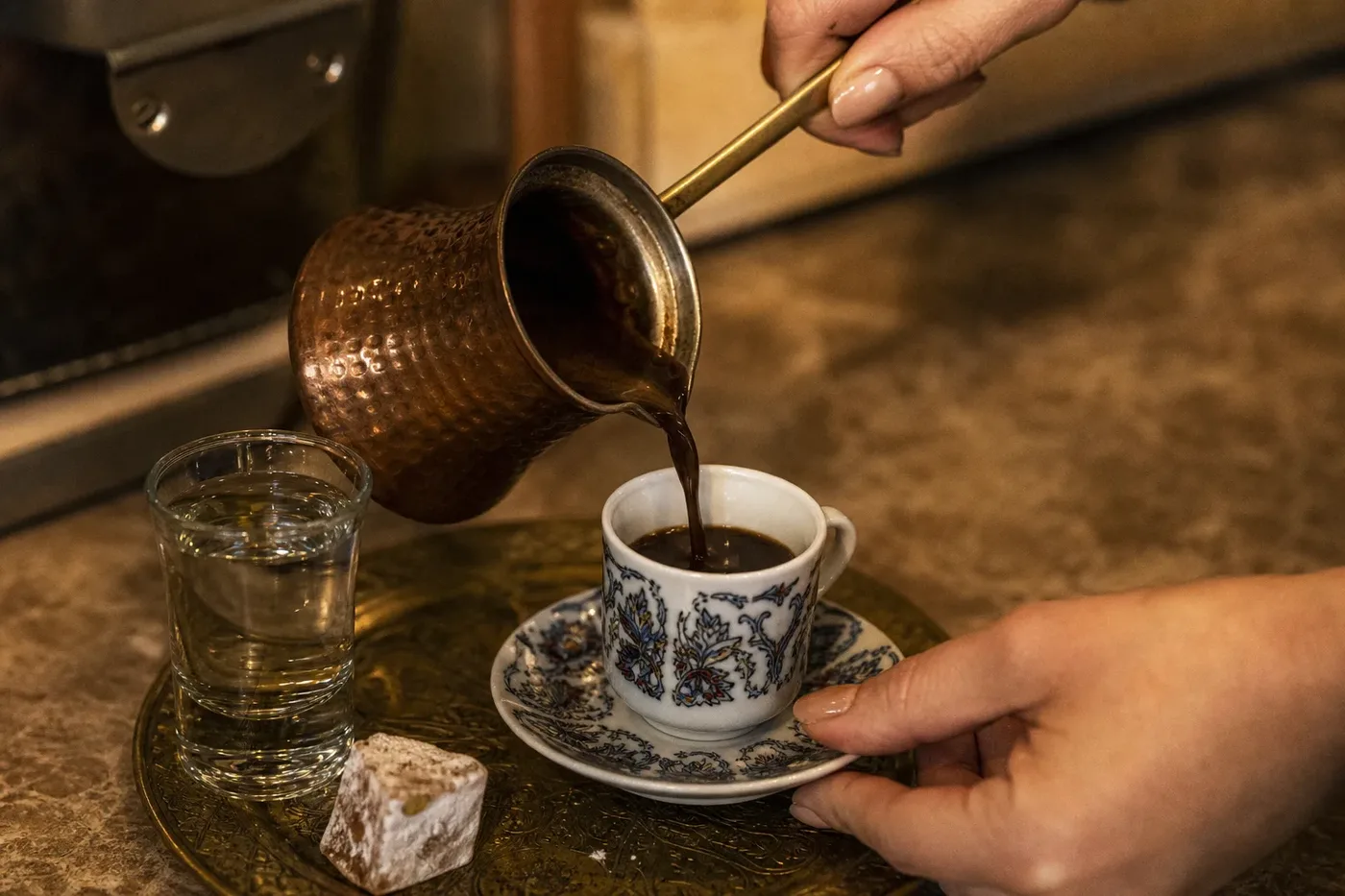 Coffee poured from a copper pot into a small porcelain cup on a brass tray