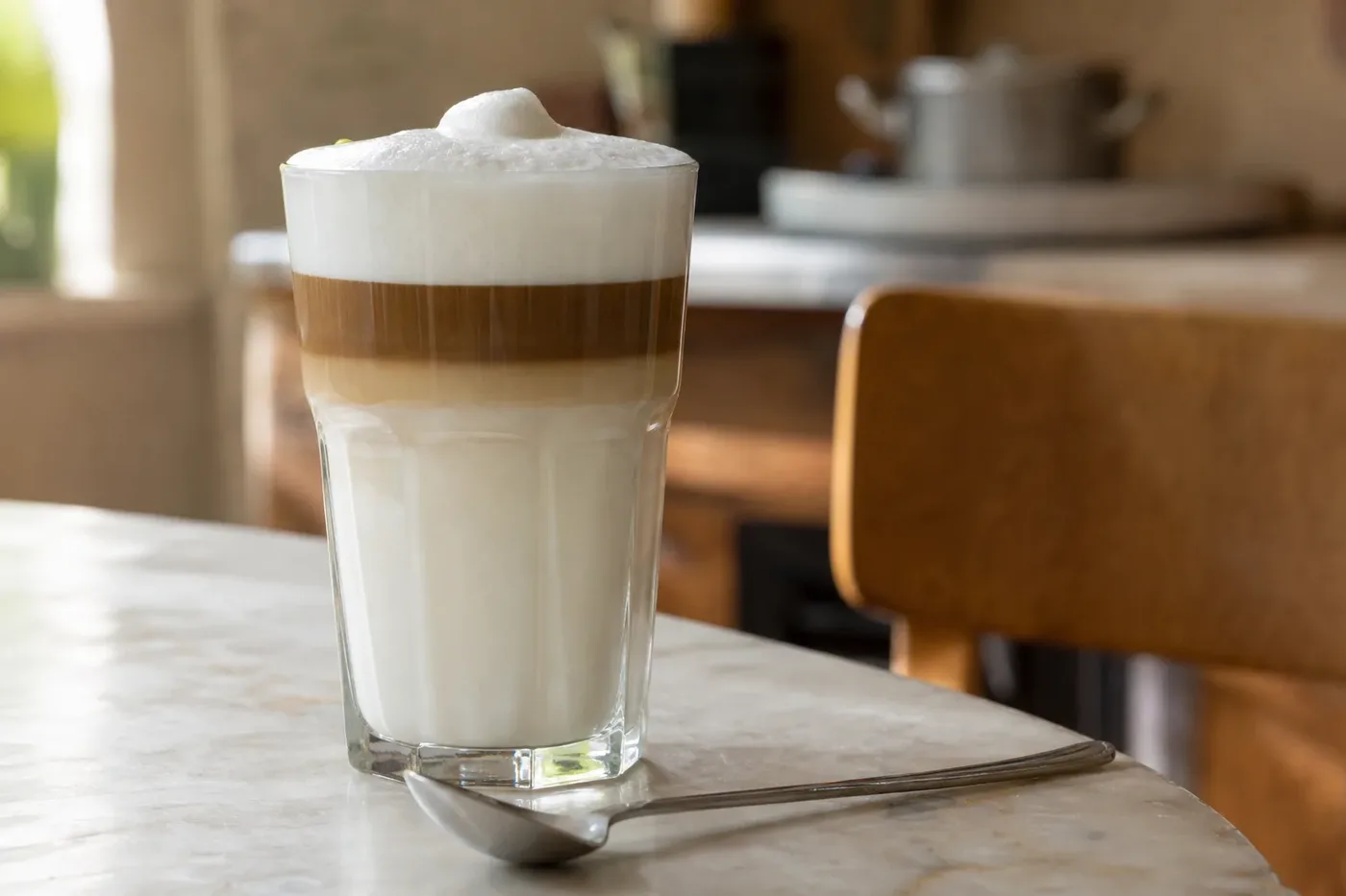 A layered latte macchiato in a tall glass with bands of milk, espresso and foam
