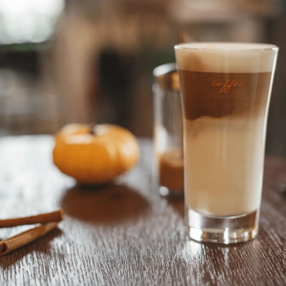 a glass of cinnamon spice coffee with cinnamon sticks and pumpkin on a table