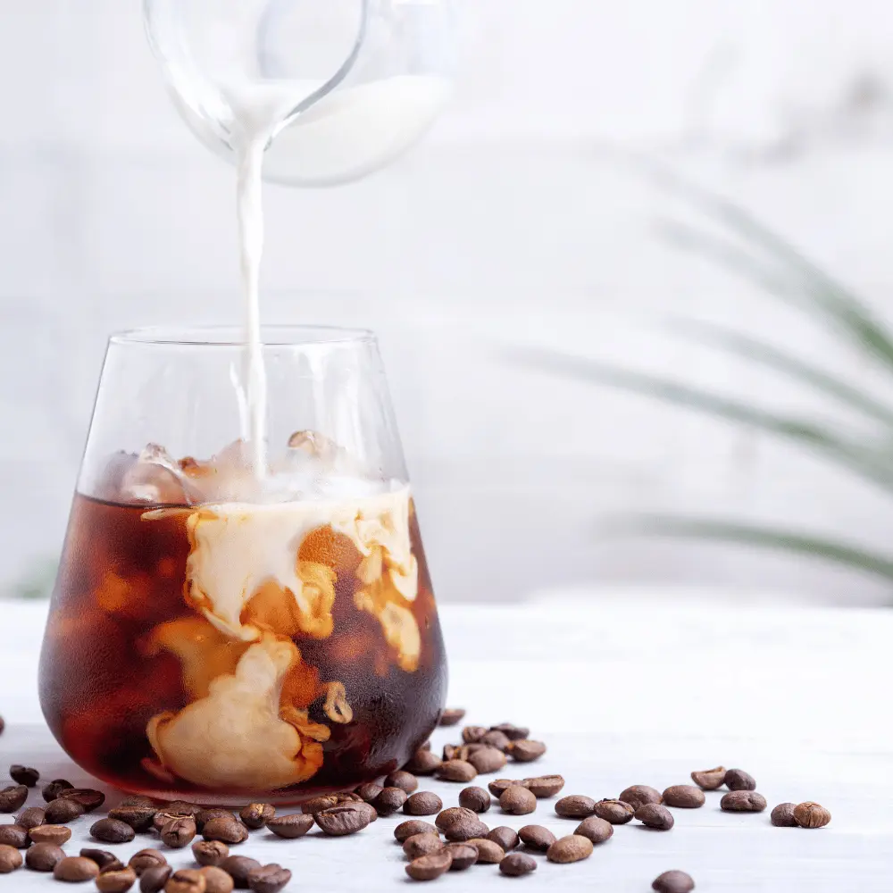 pouring milk into a glass of cold brew coffee with roasted coffee beans