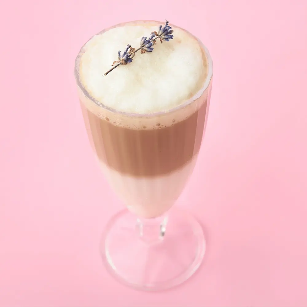 a lavender latte in a tall glass topped with a lavender garnish