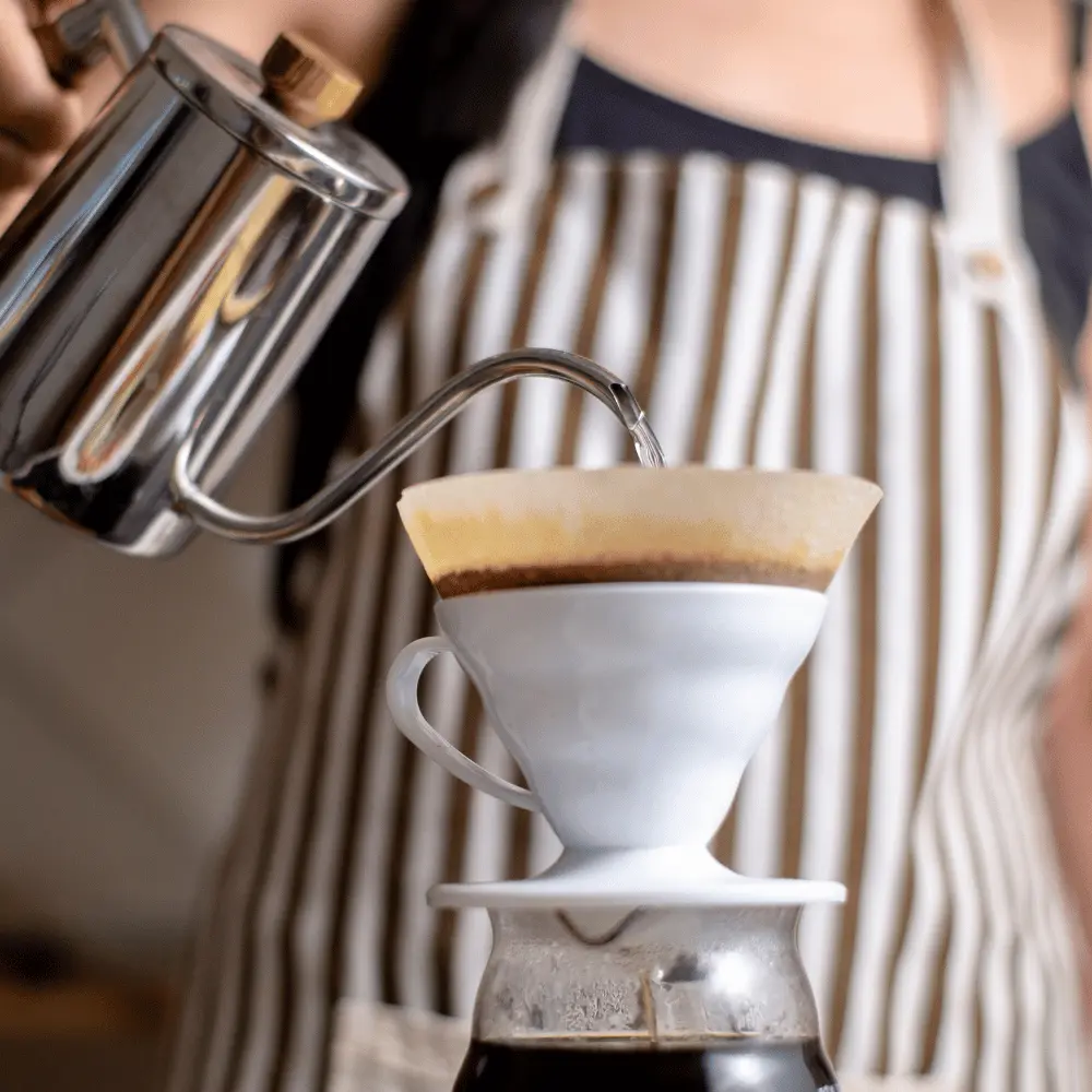 woman pouring water from a gooseneck kettle to brew pour over coffee
