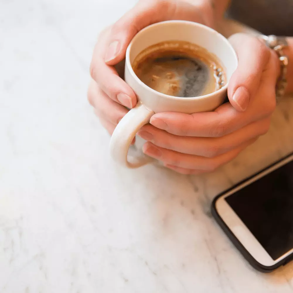 woman holding a cup of java with a smartphone on a table