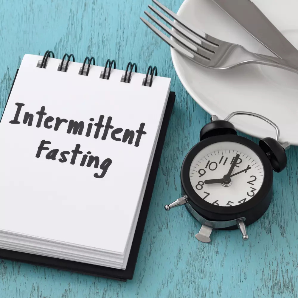 a word of intermittent fasting on a notepad with clock and kitchen utensils