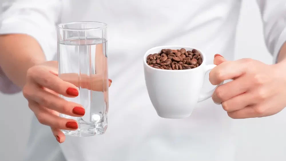woman holding a glass of water and a cup of coffee beans