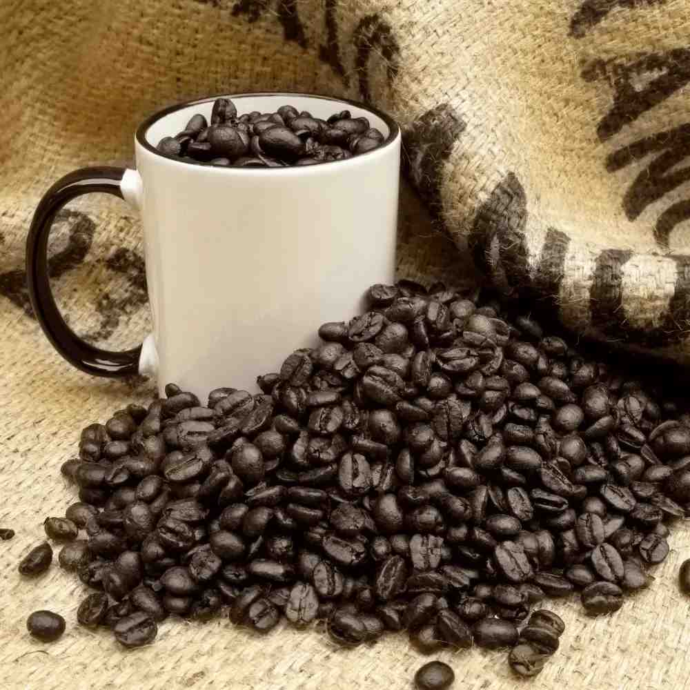 a cup of dark roasted oily coffee beans in a mug on a hemp bag