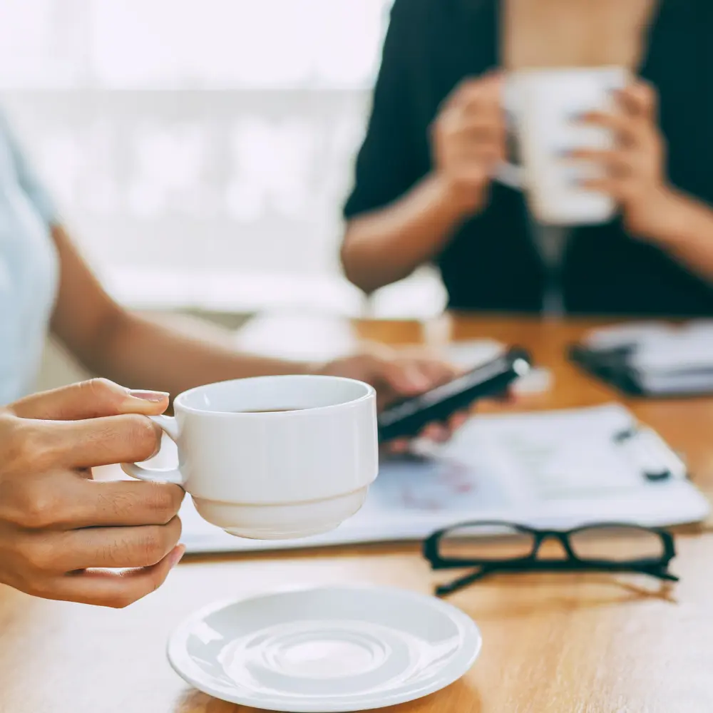 two workers having coffee at a desk and discussing work details