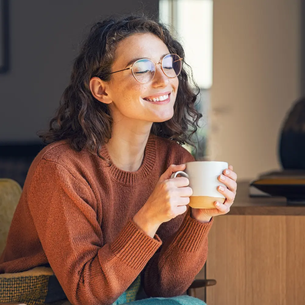 young woman smiling as she enjoys her morning cup of coffee