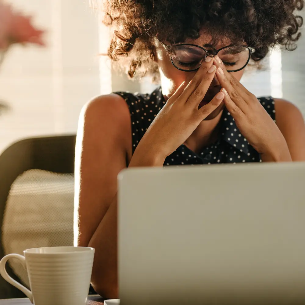 a woman working on her laptop, drinking coffee stressed because of her underactive thyroid