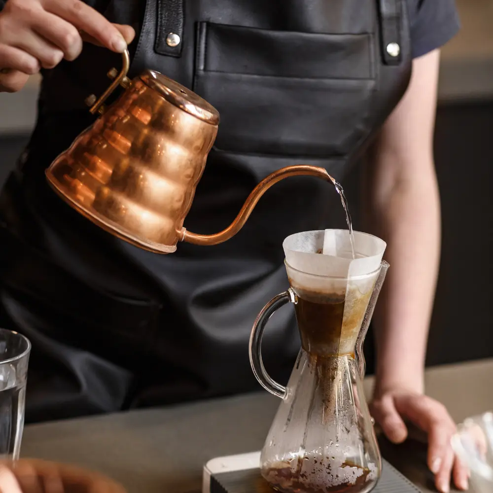 barista brewing pour over coffee with a gooseneck kettle