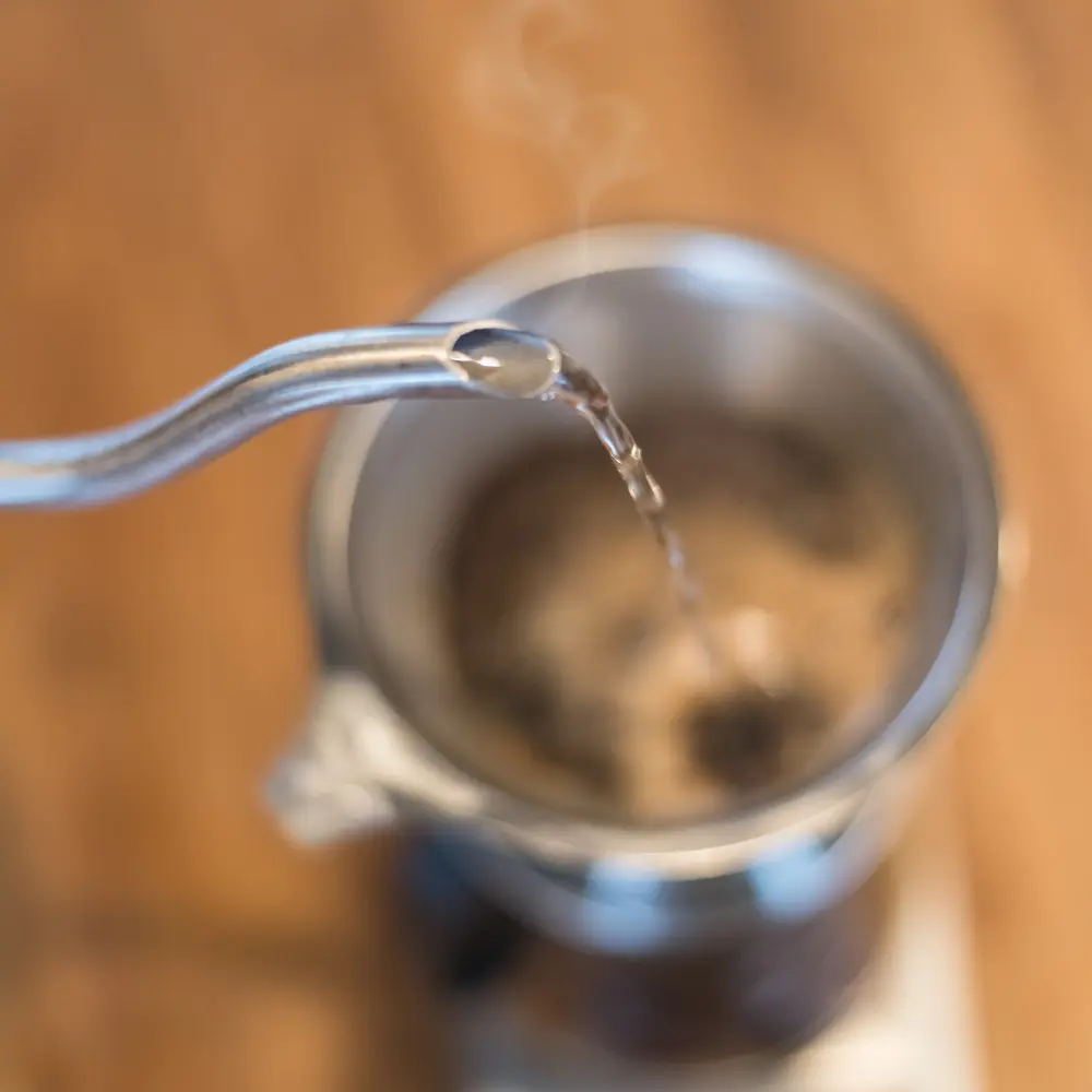 gooseneck kettle pouring water slowly over coffee grounds