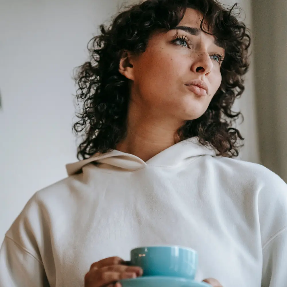 a woman looking out in the distance and drinking her coffee