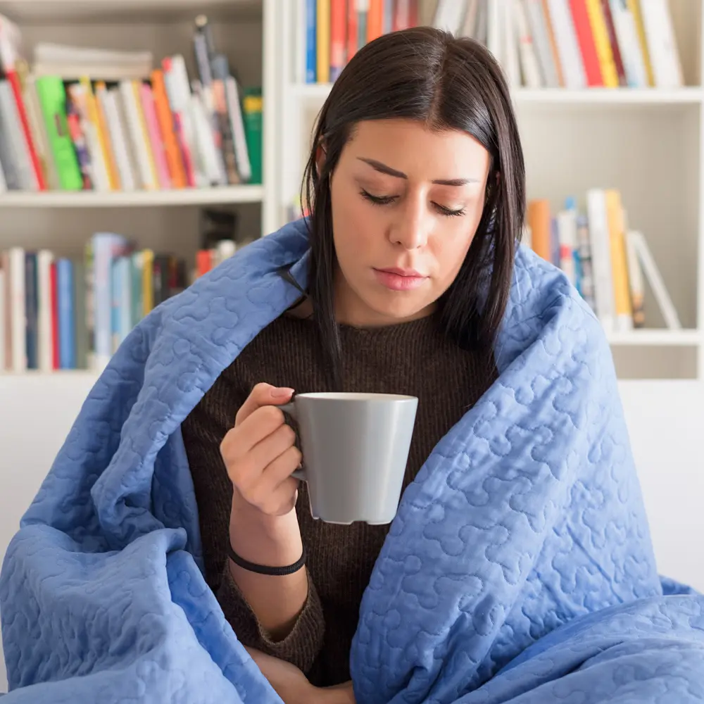 a woman covered in her blanket worried about her thyroid while drinking her coffee