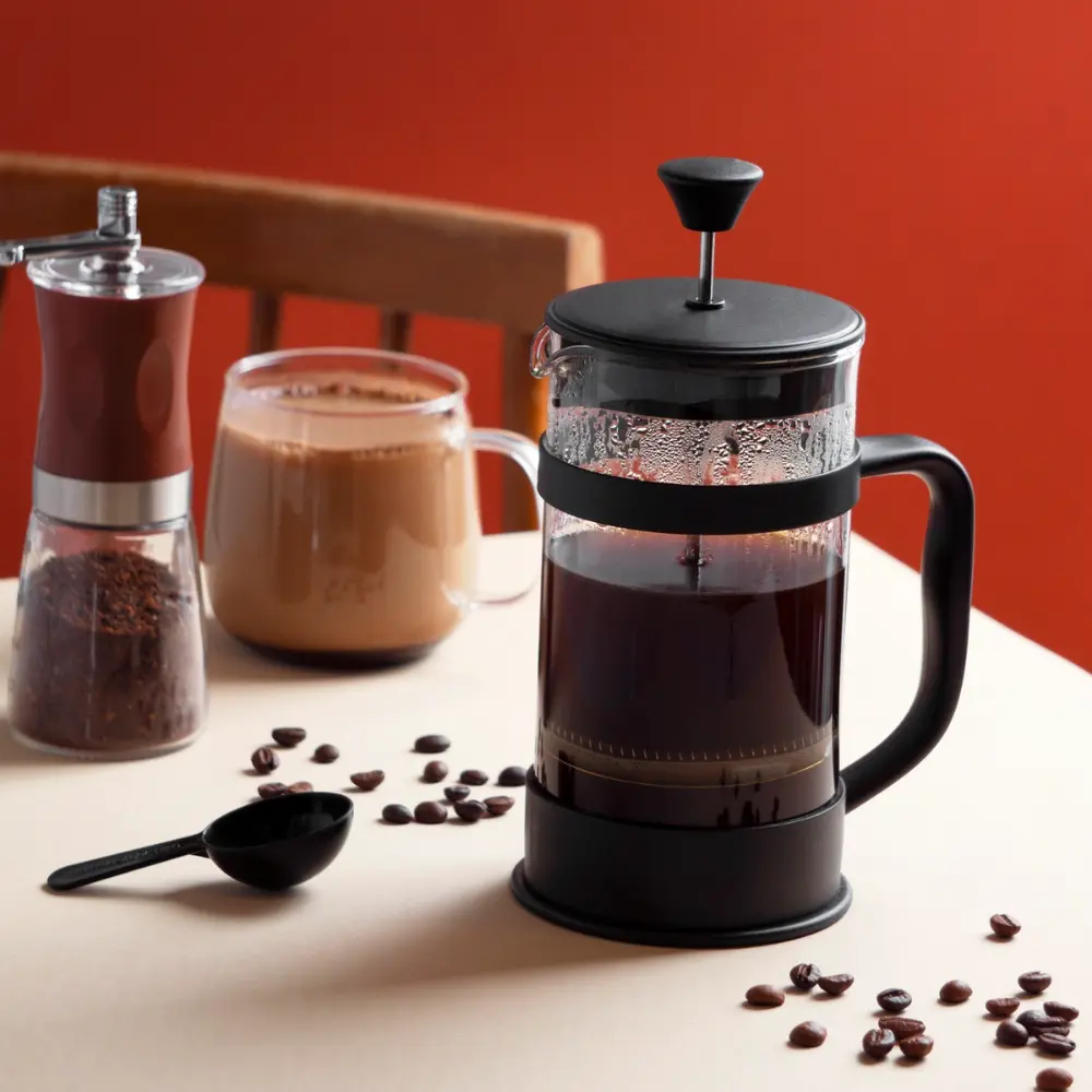 french press coffee maker on a table with coffee beans and a cup