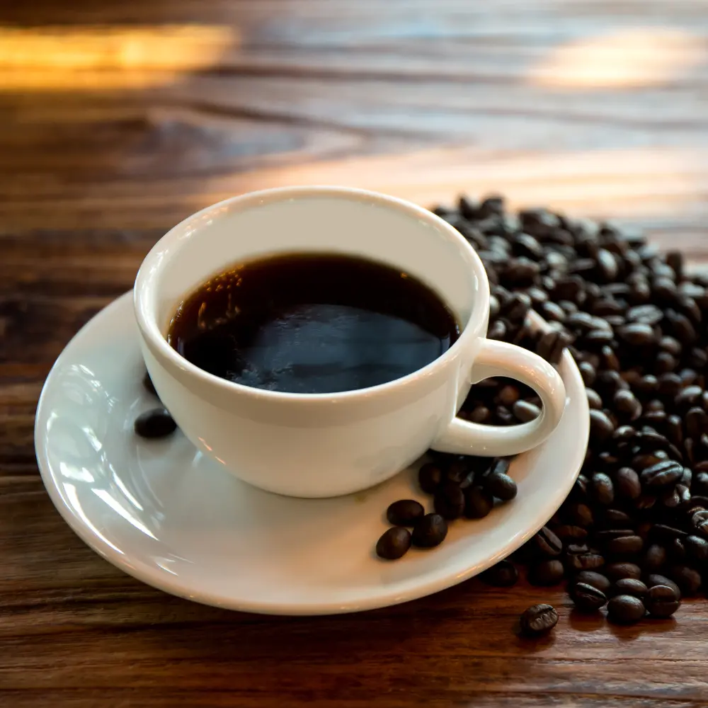 black americano in a white mug and saucer with beans