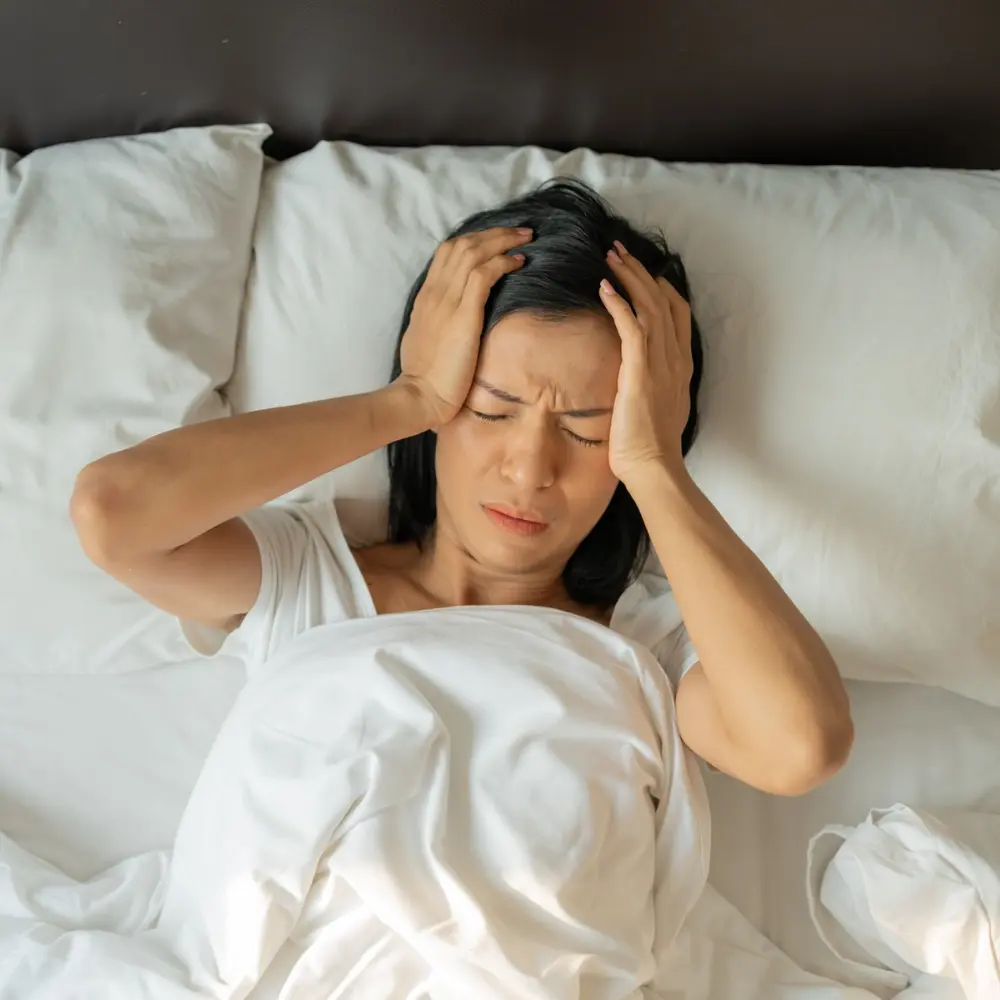 woman holding her head in pain while laying in bed