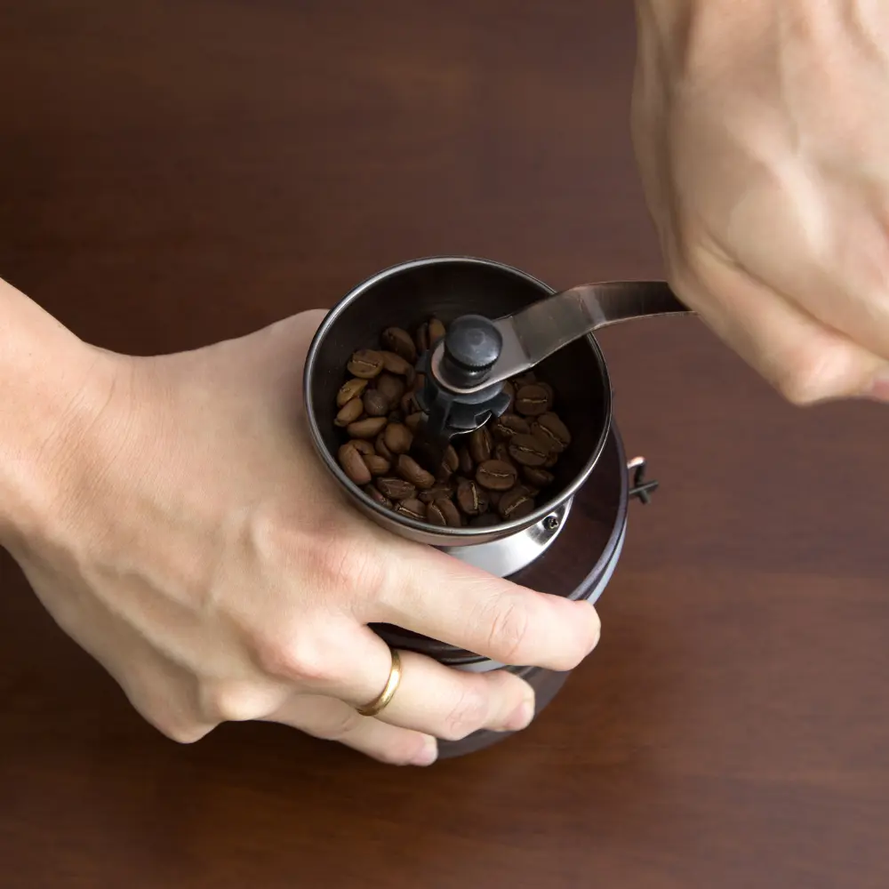 person using a handheld burr coffee grinder