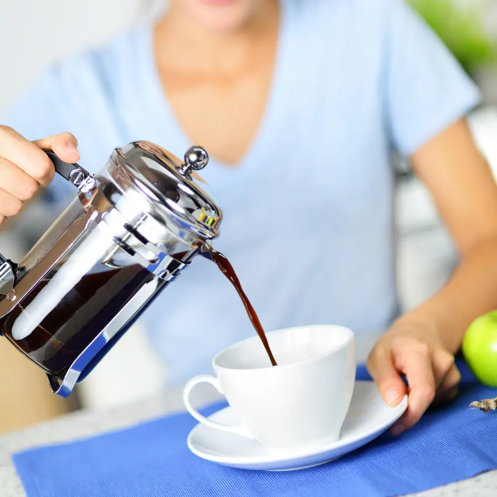 woman pouring french press steeped coffee into a white mug