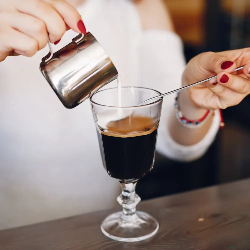 person adding milk to an americano
