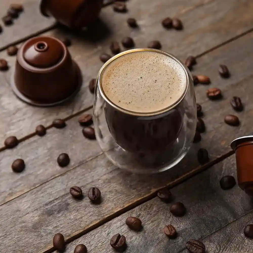 a glass mug of black coffee with beans around