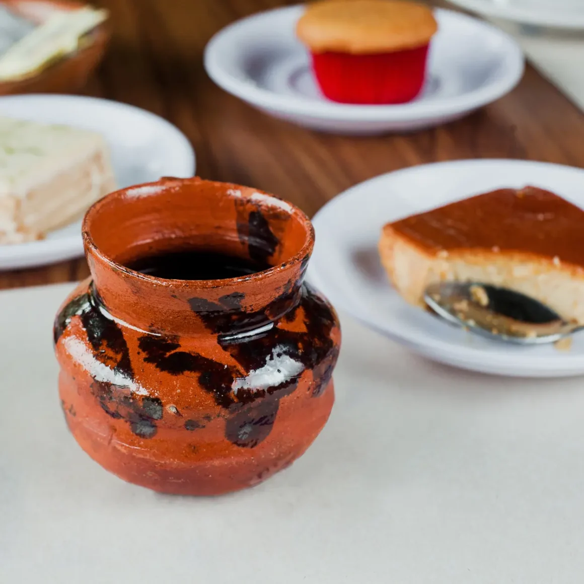 a small clay pot with cafe de olla coffee in it next to a piece of cake