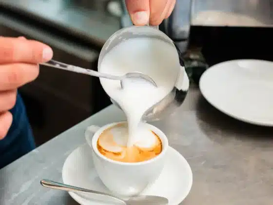 a person pouring microfoam milk into a cup of coffee