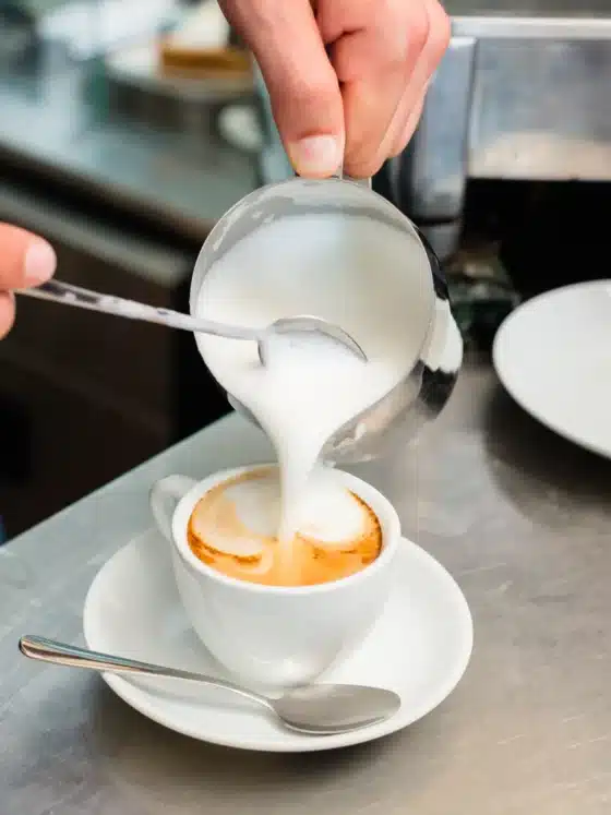 a person pouring microfoam milk into a cup of coffee