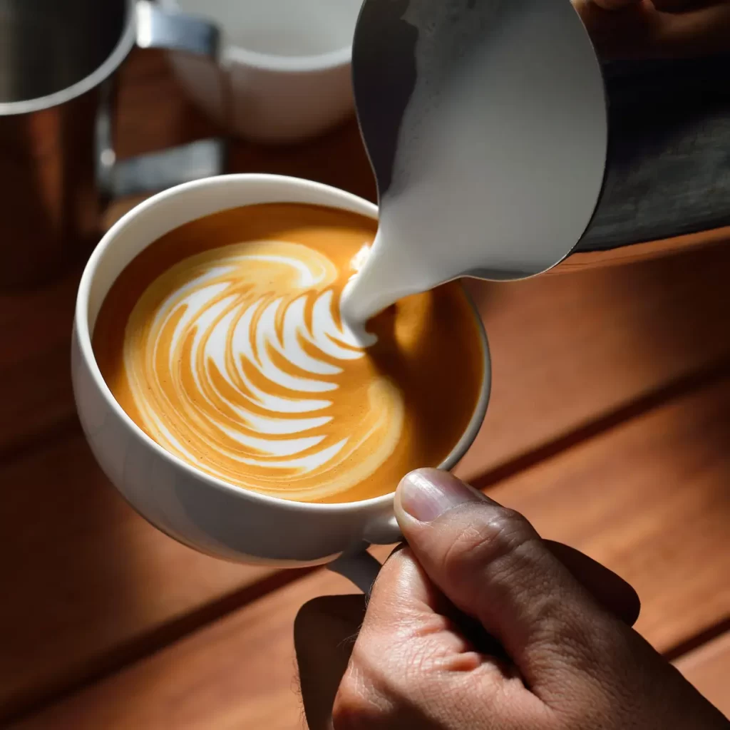 a person pouring milk into a cup of coffee