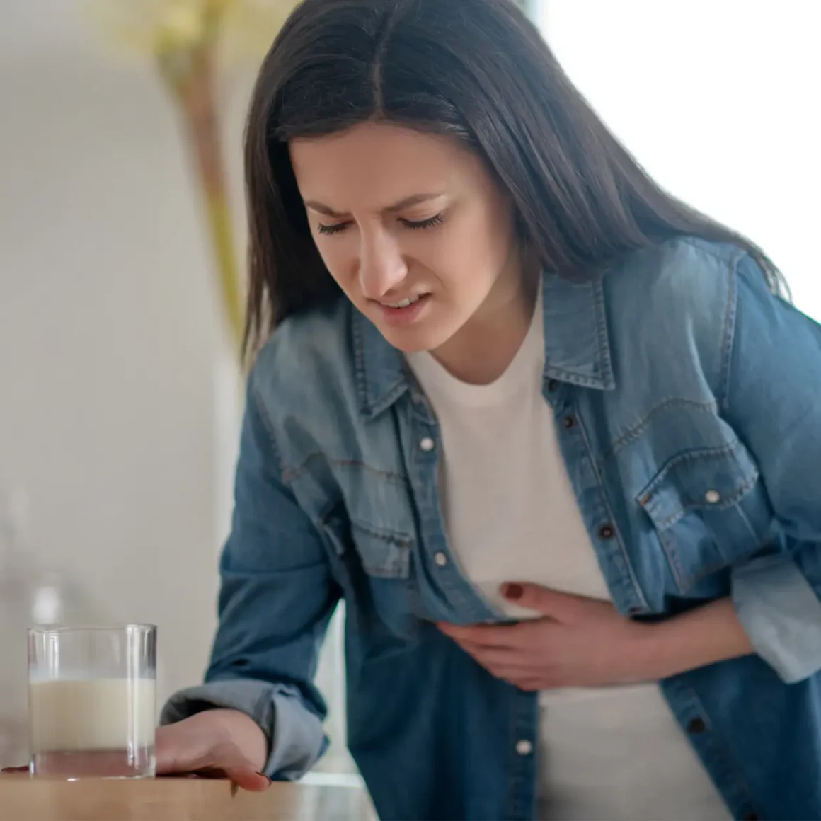 a woman holding her stomach and looking at a glass of milk