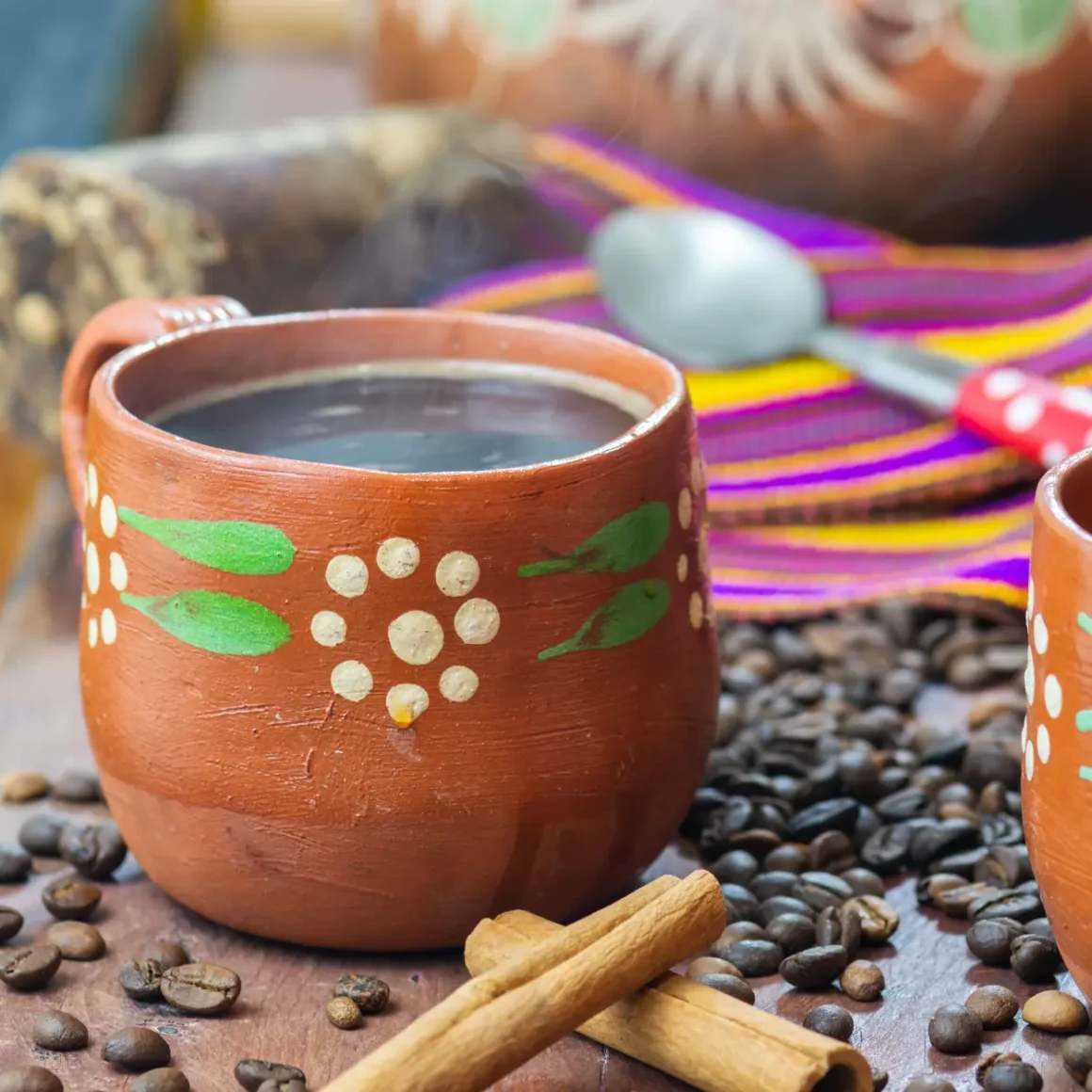 a cup of cafe de olla coffee in a clay pot with a spoon and coffee beans