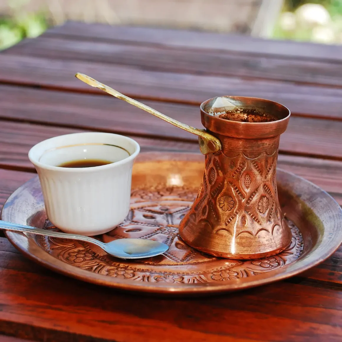 a copper pot with a cup of coffee and a spoon on a copper plate
