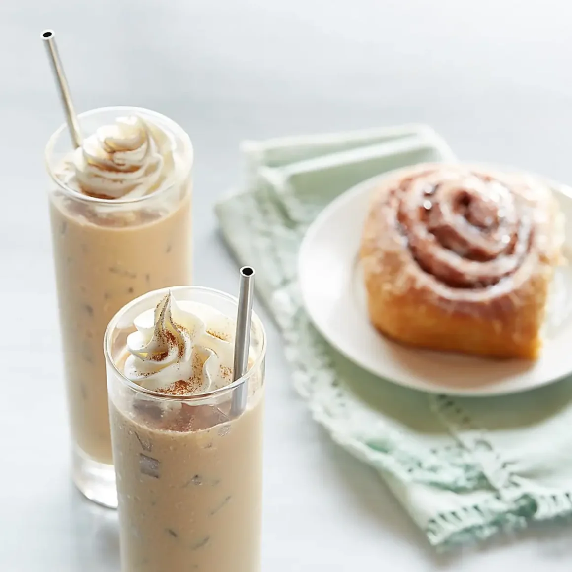 two glasses of cinnamon roll cold brew and a pastry on a plate