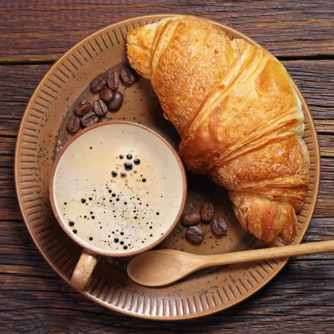 a plate with croissant and coffee beans with a cup of instant coffee