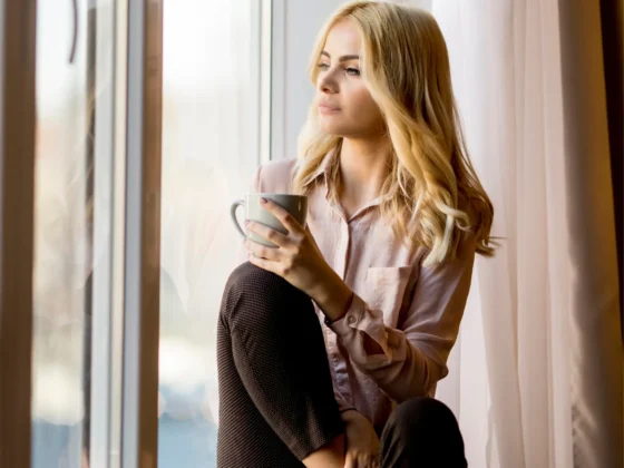 a woman sitting on a window sill holding a cup