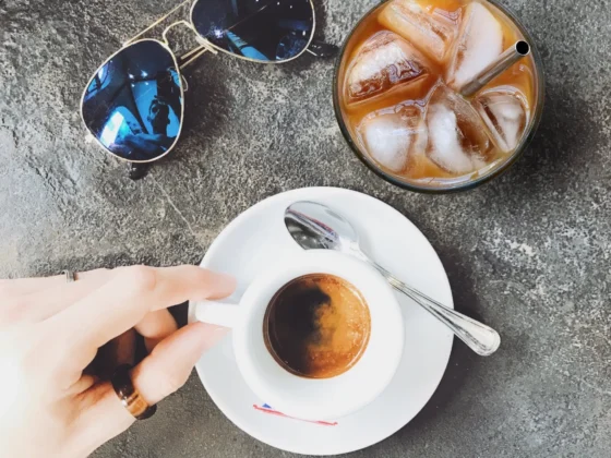 a hand holding a cup of coffee next to a glass of ice and sunglasses