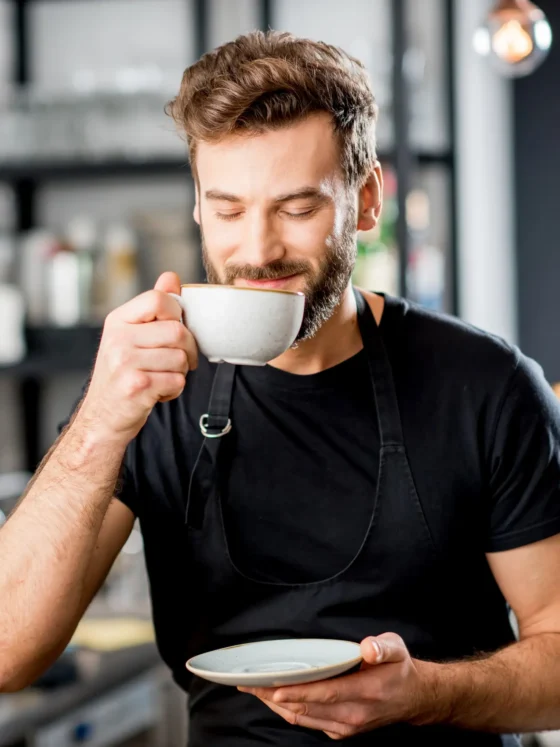 a person in a black shirt smelling a cup of coffee