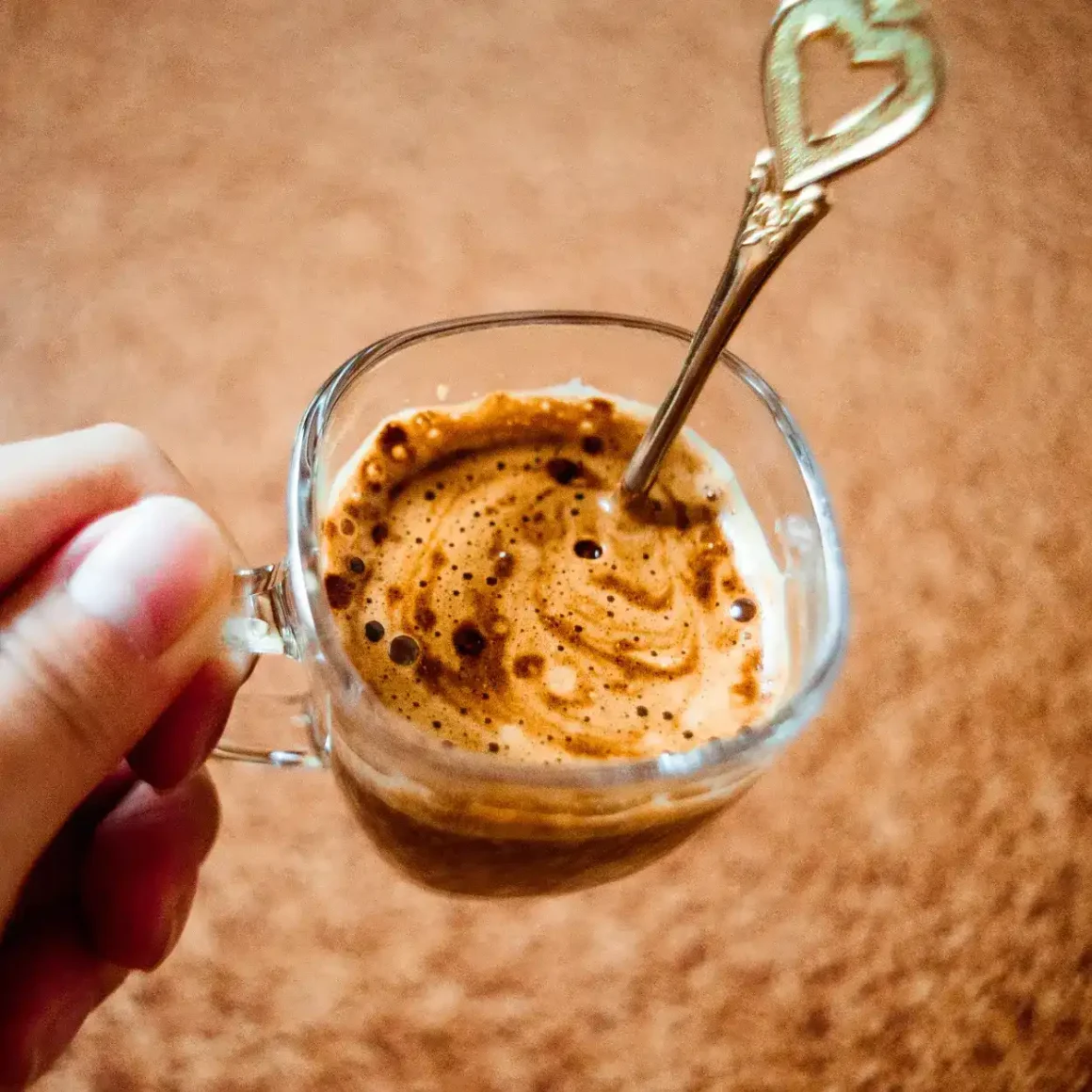 barista holding a glass cup of instant coffee with a spoon