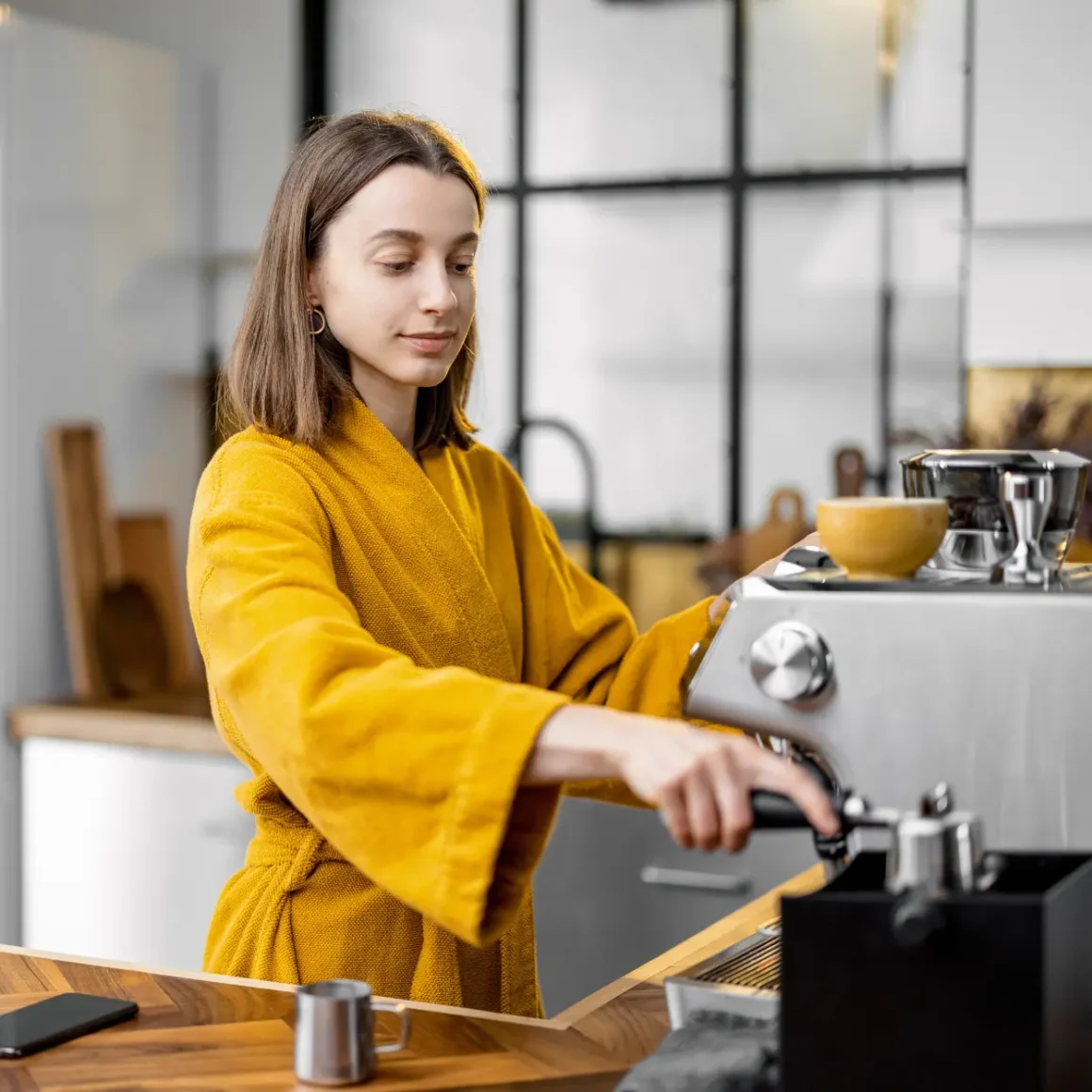 a woman in a yellow robe making a cappuccino or latte in the morning