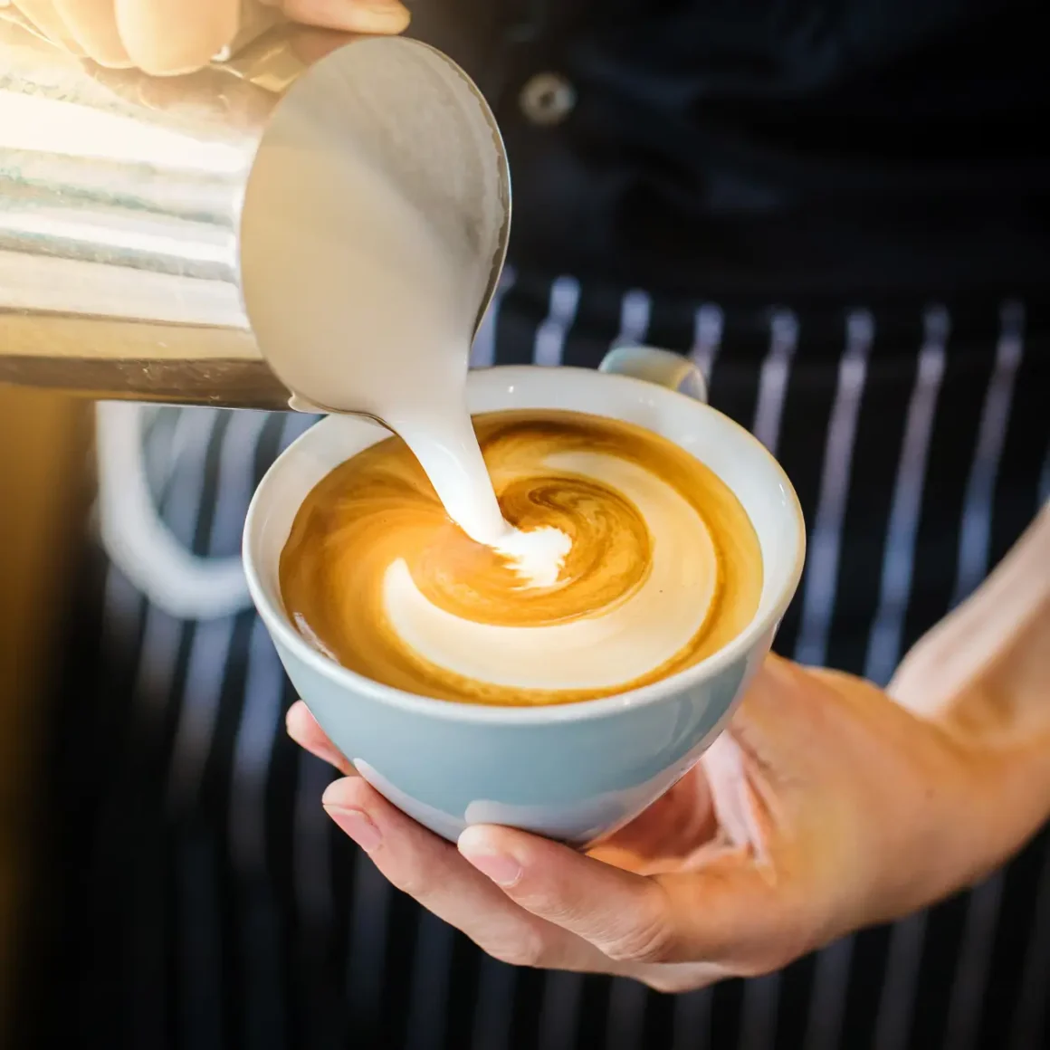 a person pouring milk into a cup of coffee