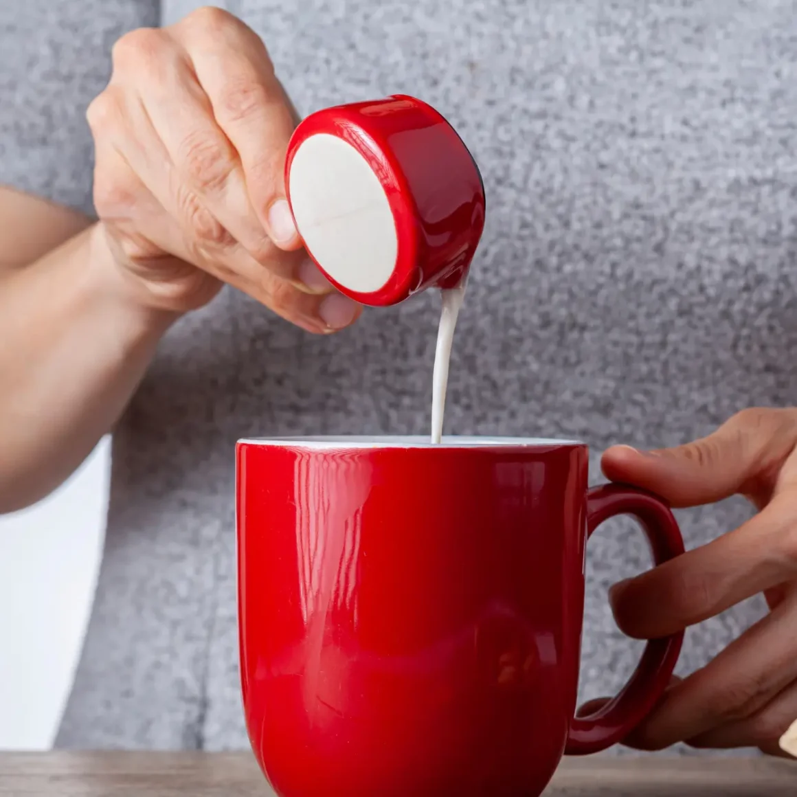 barista pouring milk into a red mug
