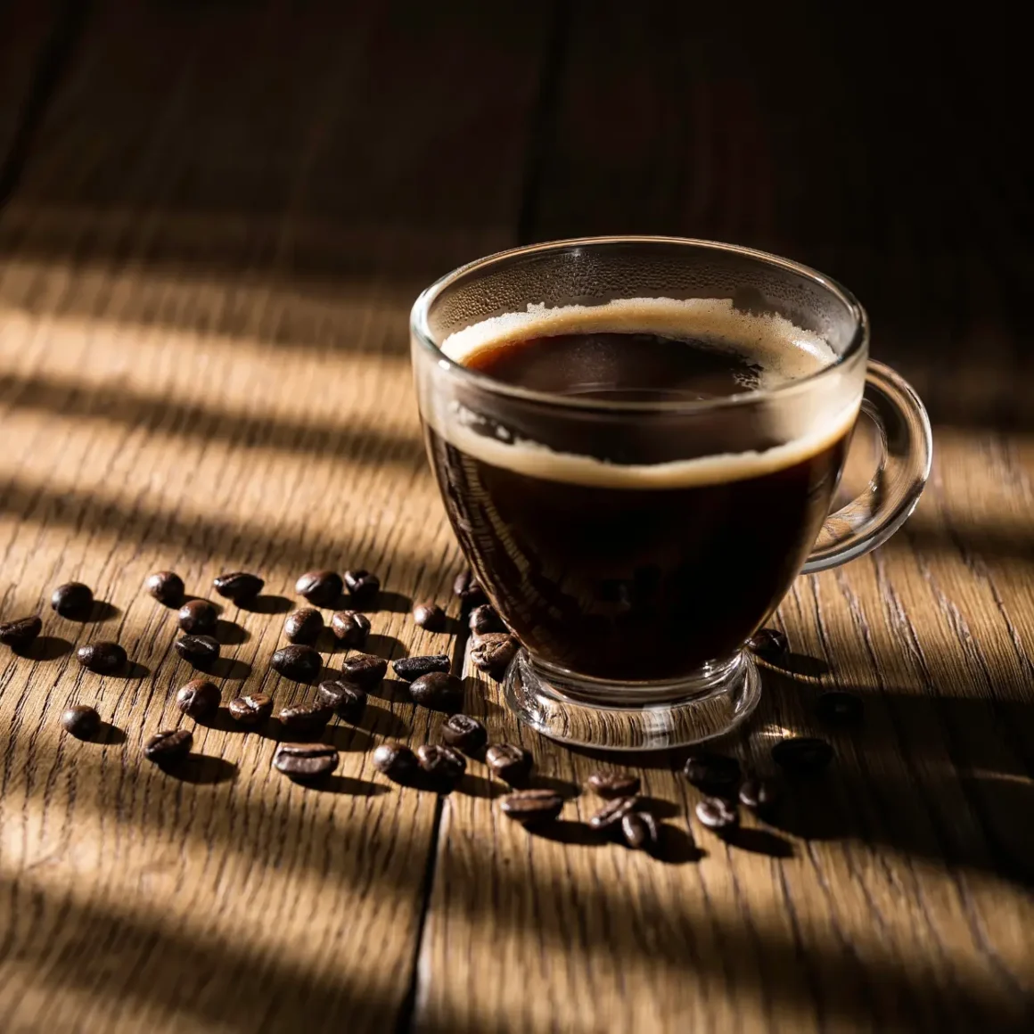 a cup of dark roast coffee and coffee beans on a table