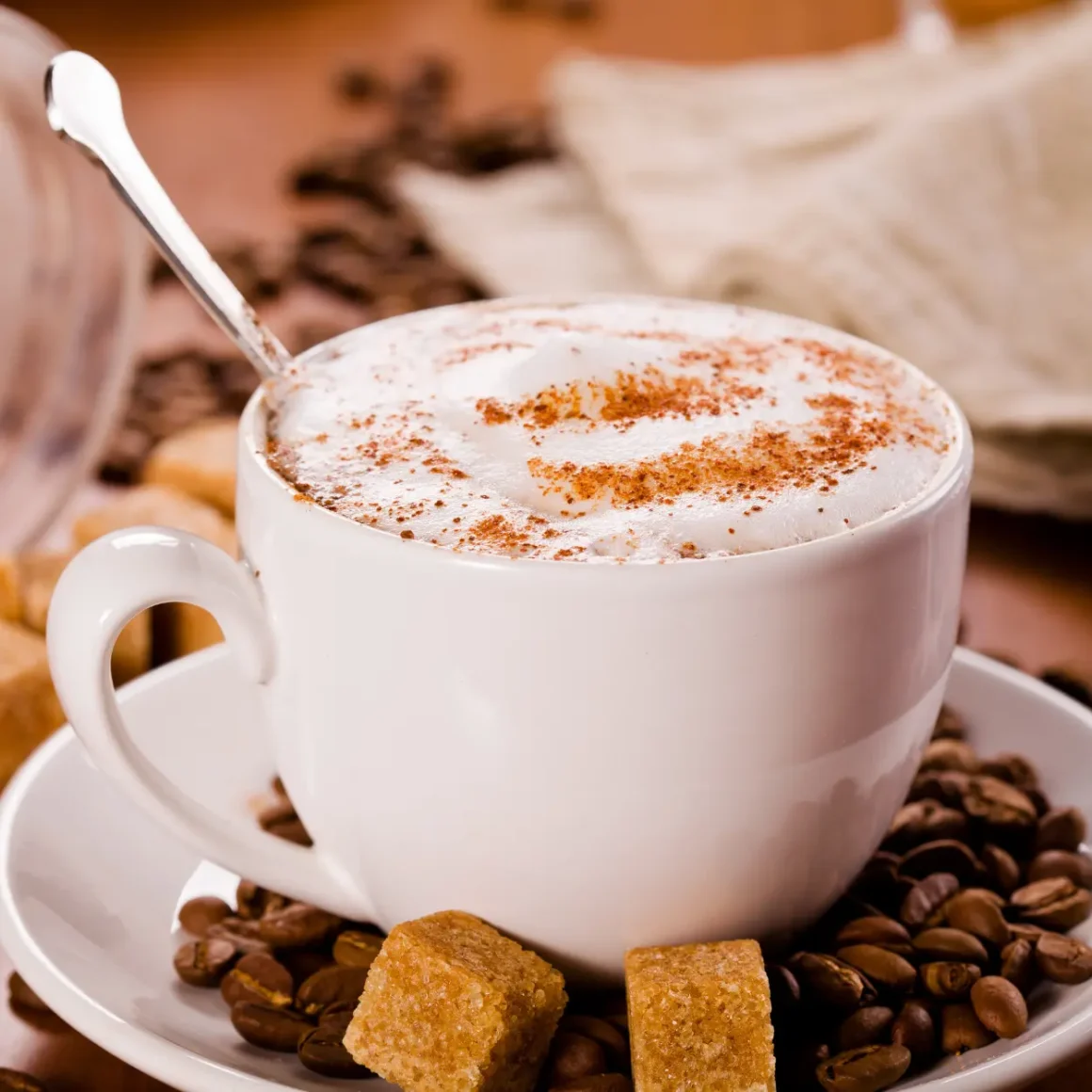 a cup of dry cappuccino with brown sugar cubes and coffee beans on a saucer