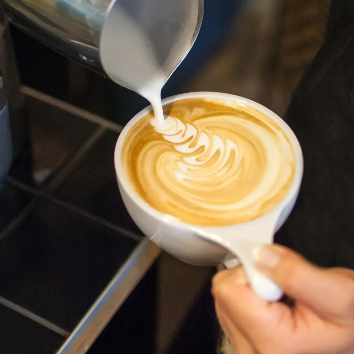 barista pouring milk into a cup of latte